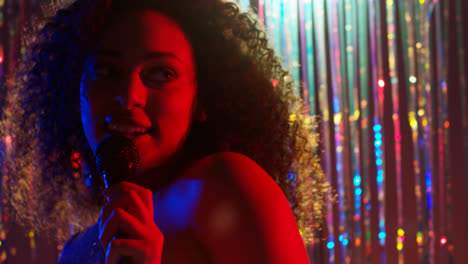 Young-Woman-With-Microphone-Singing-At-Karaoke-Nightclub-Bar-Or-Disco-With-Sparkling-Lights-In-Background-1